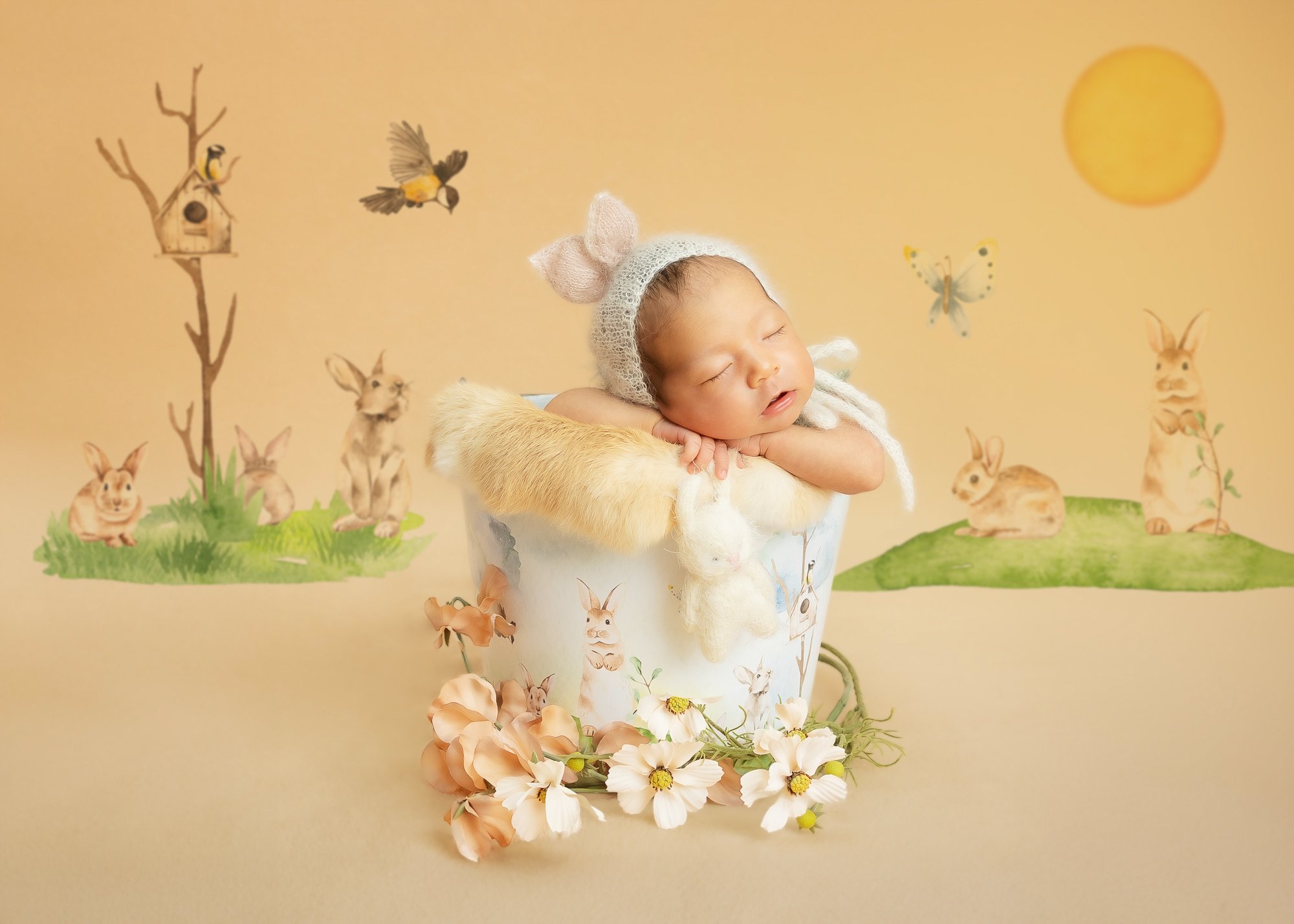 Newborn in bunny-ear bonnet in painted rabbit-themed bucket with storybook background — IDTPhoto Chicagoland