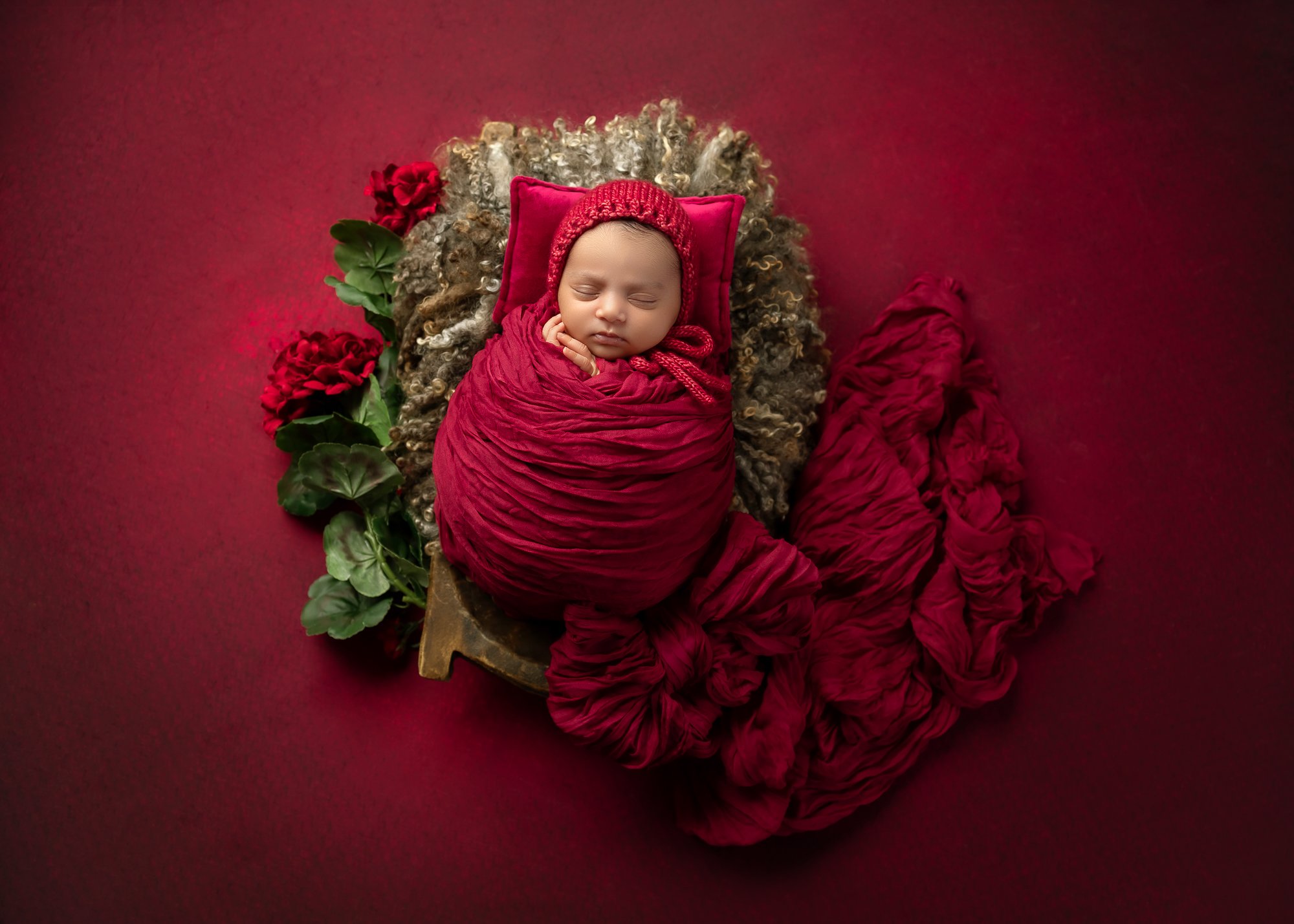 Newborn wrapped in crimson with red roses and handcrafted bonnet — IDTPhoto