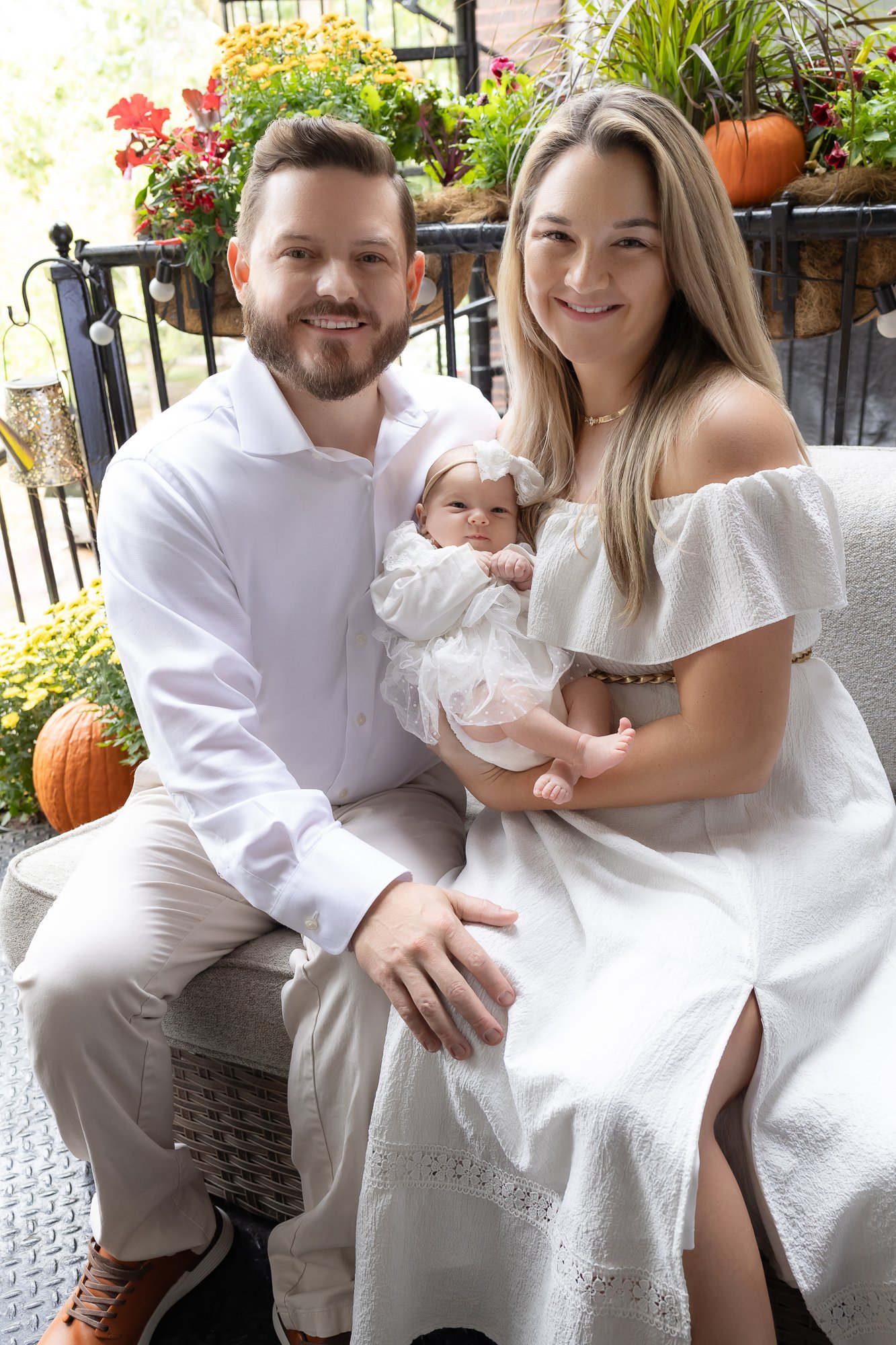 Parents with newborn girl on outdoor porch surrounded by fall flowers — IDTPhoto Aurora IL lifestyle newborn photographer