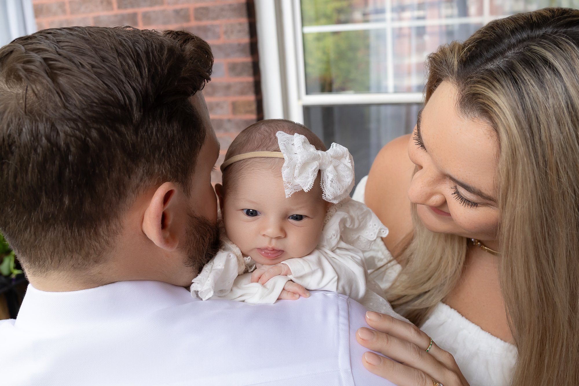 Parents from behind with newborn girl looking at camera over dad's shoulder — IDTPhoto Chicagoland lifestyle newborn