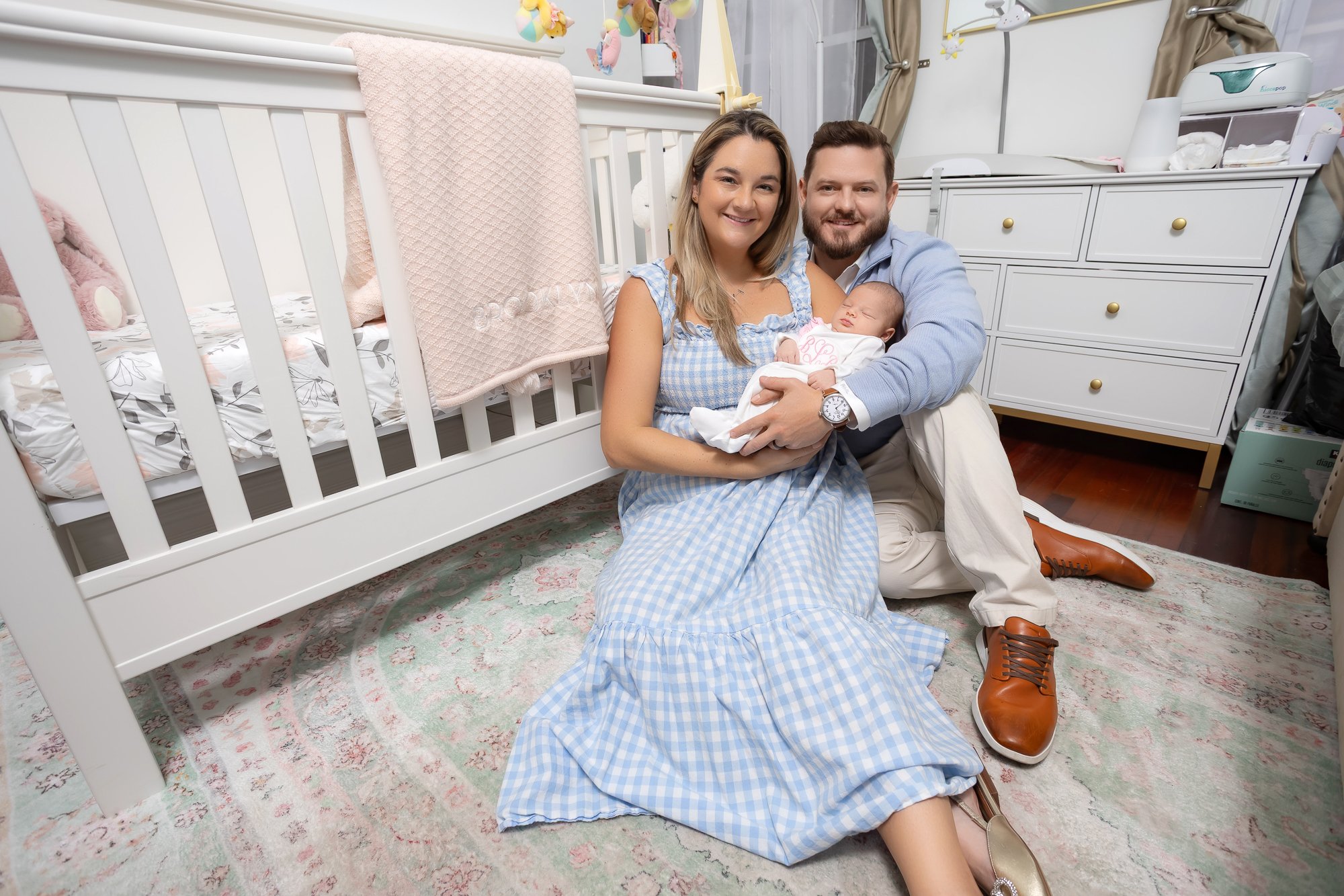 Parents sitting on nursery floor holding newborn and smiling at camera — IDTPhoto Aurora IL lifestyle newborn photographer
