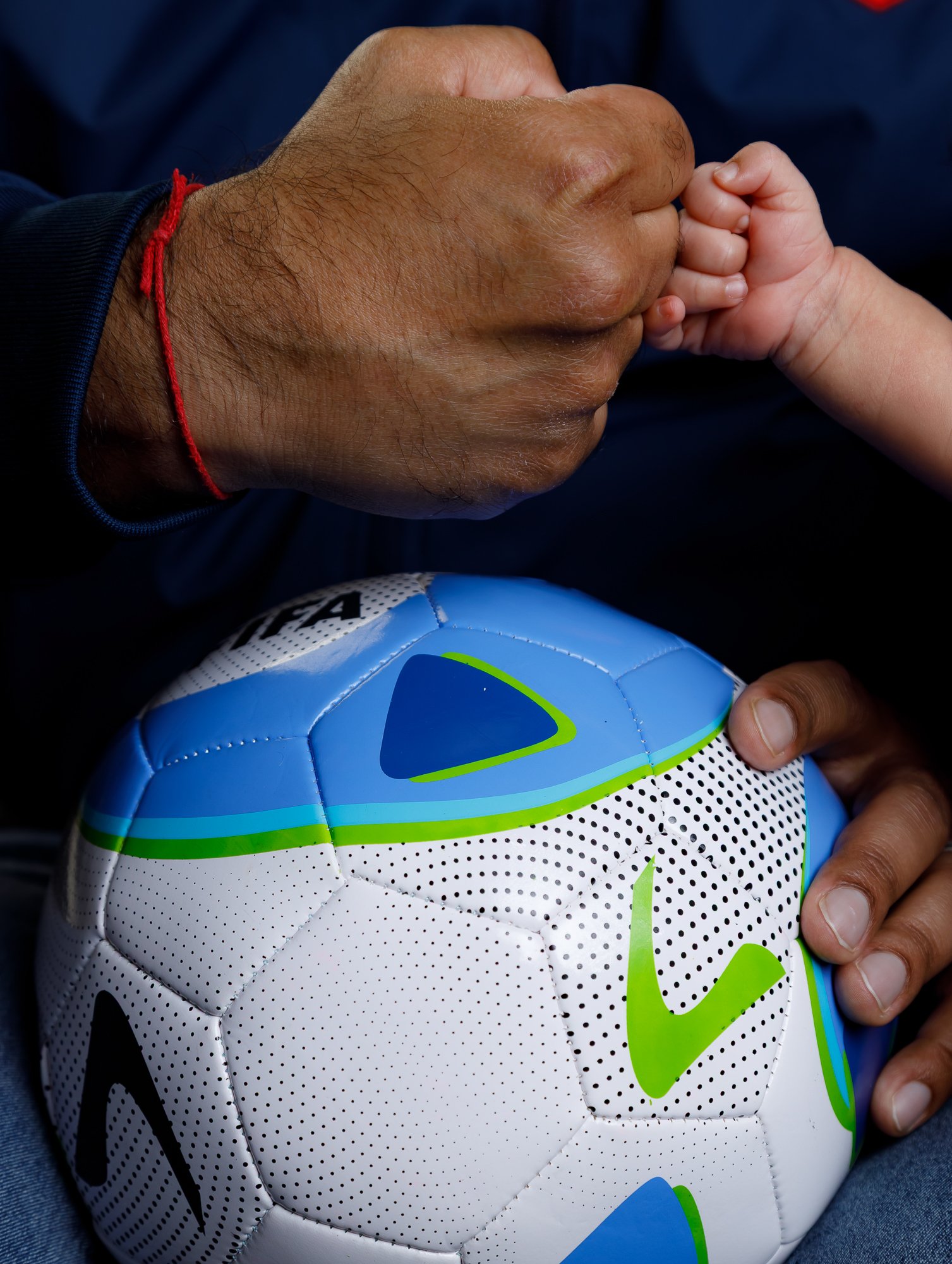 Newborn fist bump with dad's hand over soccer ball — IDTPhoto Aurora IL newborn photographer