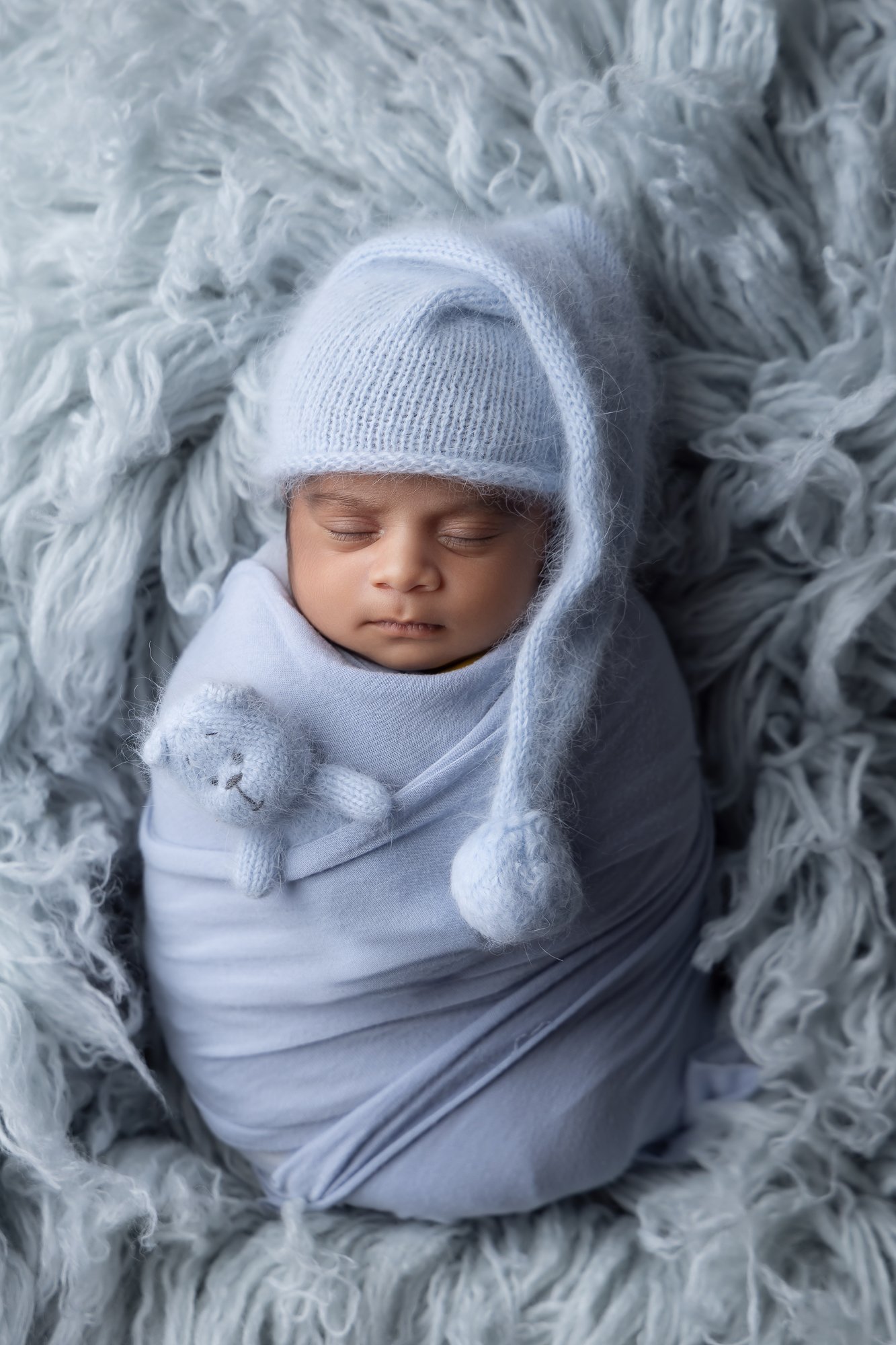 Newborn in powder blue knit wrap with sleep cap and tiny bear — IDTPhoto Chicagoland newborn studio